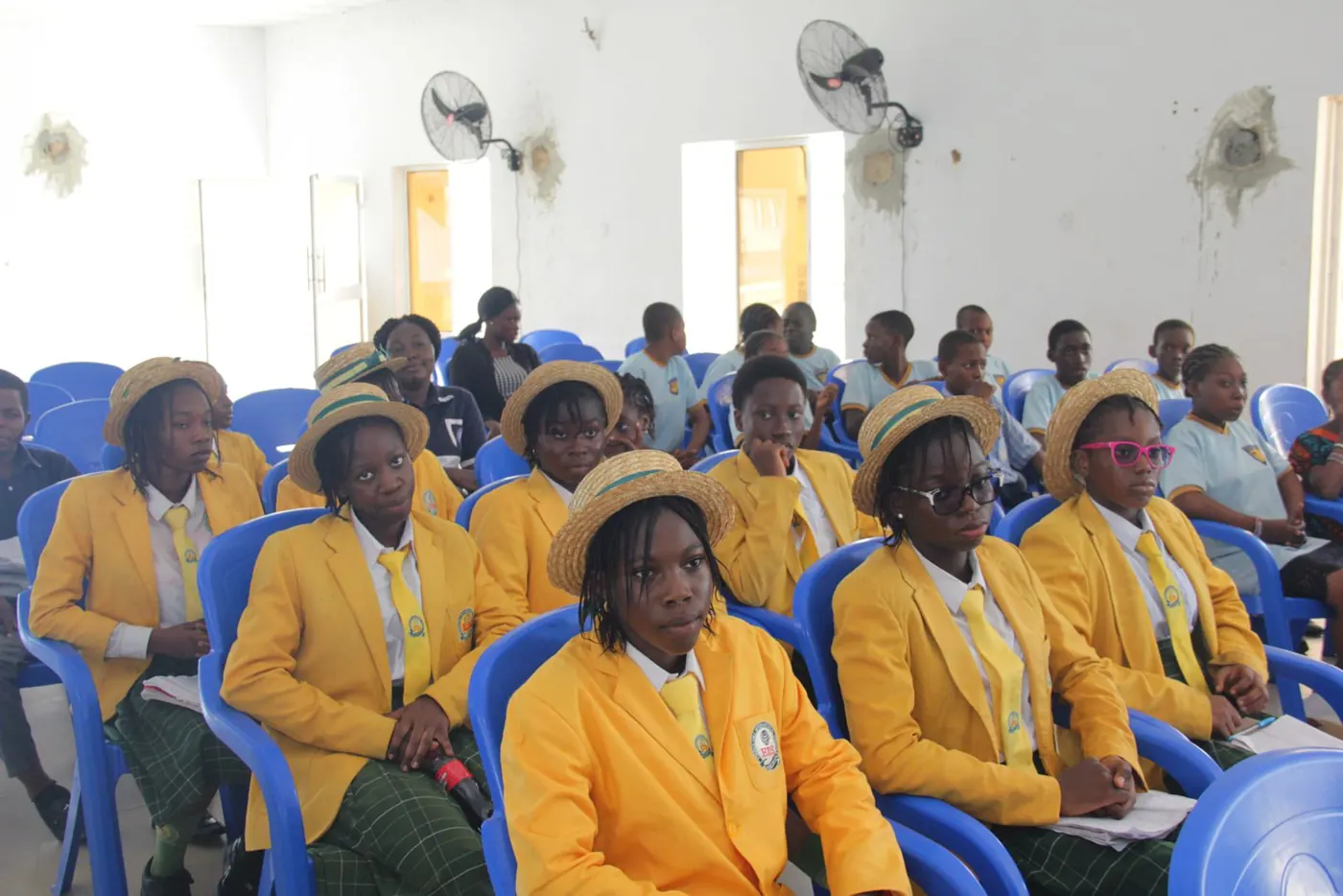 Girls in yellow blazers and straw hats seated together at a Project GIRL Again event
