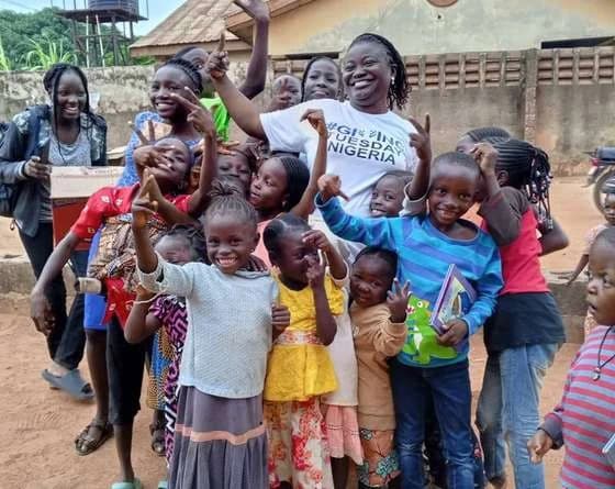 Children and volunteers cheering together outdoors, one volunteer in a GivingTuesday Nigeria T-shirt