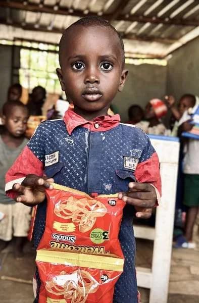 A young boy smiling and holding a snack packet