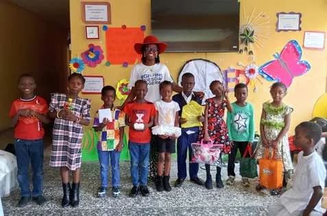 Children posing with a volunteer in a red hat in a brightly decorated classroom