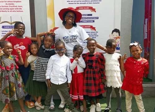 Pupils in red and white outfits posing with a volunteer in a GivingTuesday Nigeria T-shirt