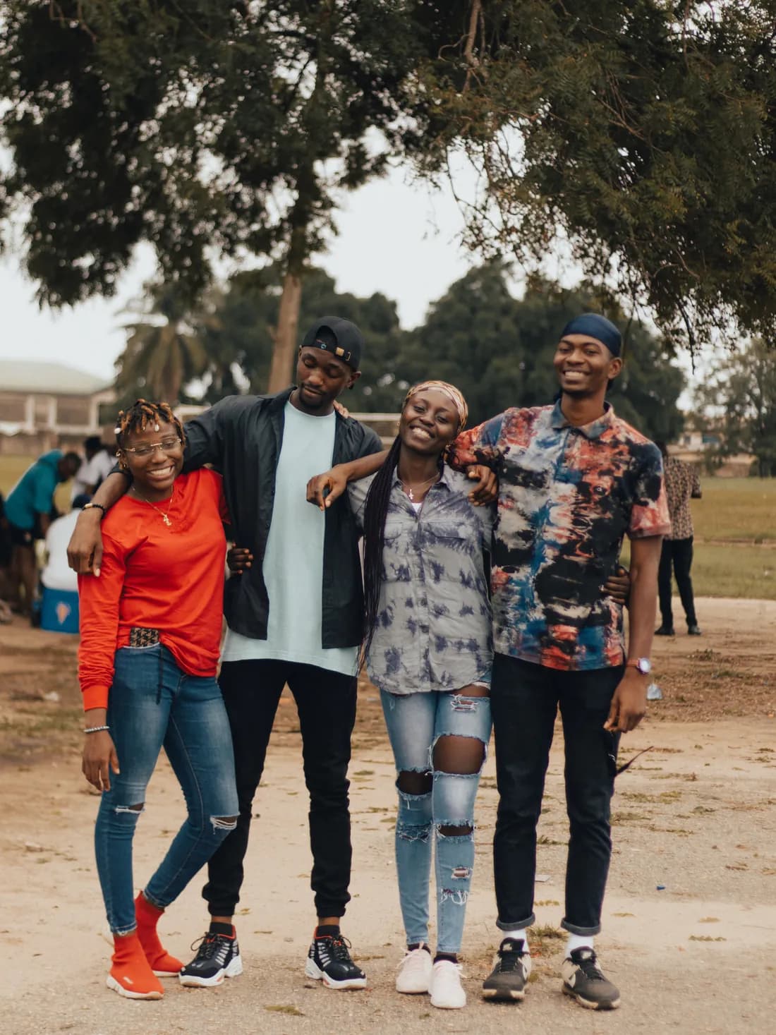 Four young people laughing together outdoors with their arms around each other